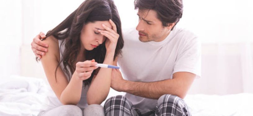 Couple dreaming to be parents. Upset man comforting his depressed wife with negative pregnancy test, free space