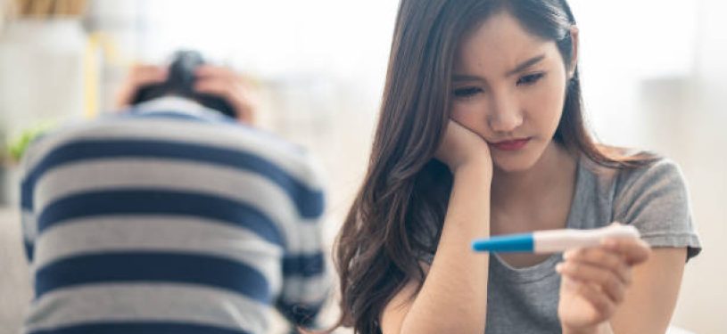 Disappointed Asian woman sitting bed when see the pregnancy test result. Girl feels worry and not ready to be a mother. Man feeling stress about the future kid holding head. Unprepared sexual problem.