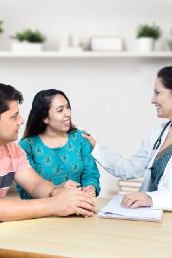 Indian female gynecologist doctor consulting young married couple patients in fertility clinic about IVF or IUI. Planning pregnancy concept.